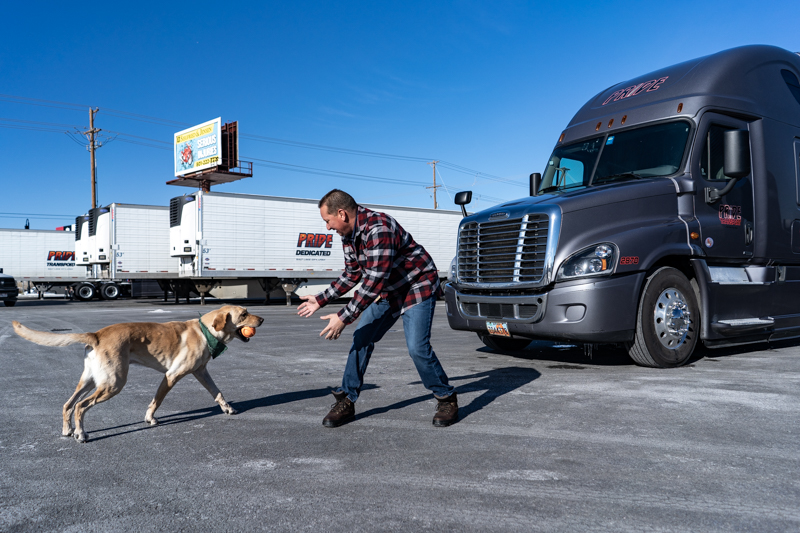 man and dog playing near semi trucks