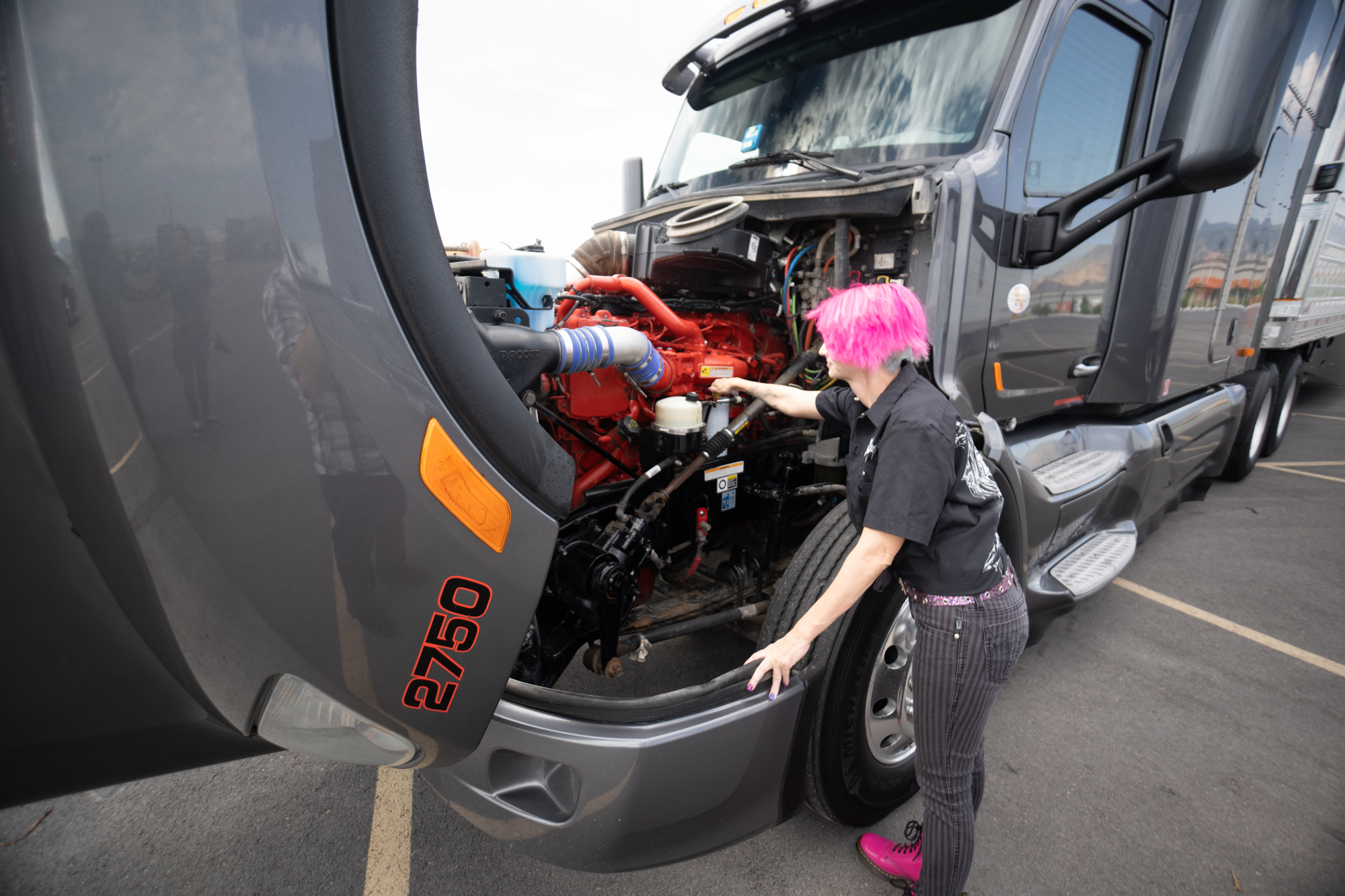 female truck driver looking under hood of truck