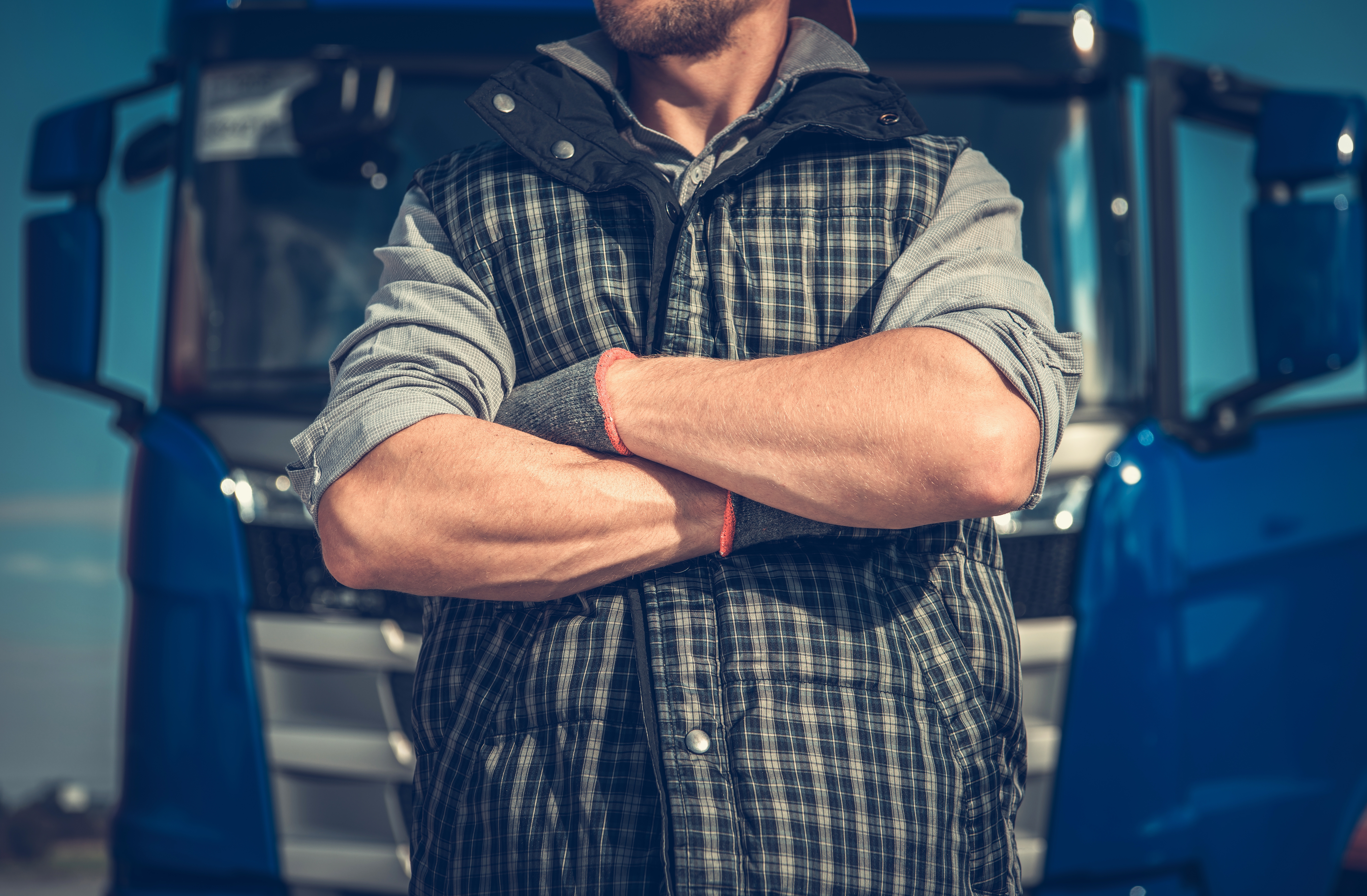 man standing in front of truck with arms crossed and head cropped out of the photo