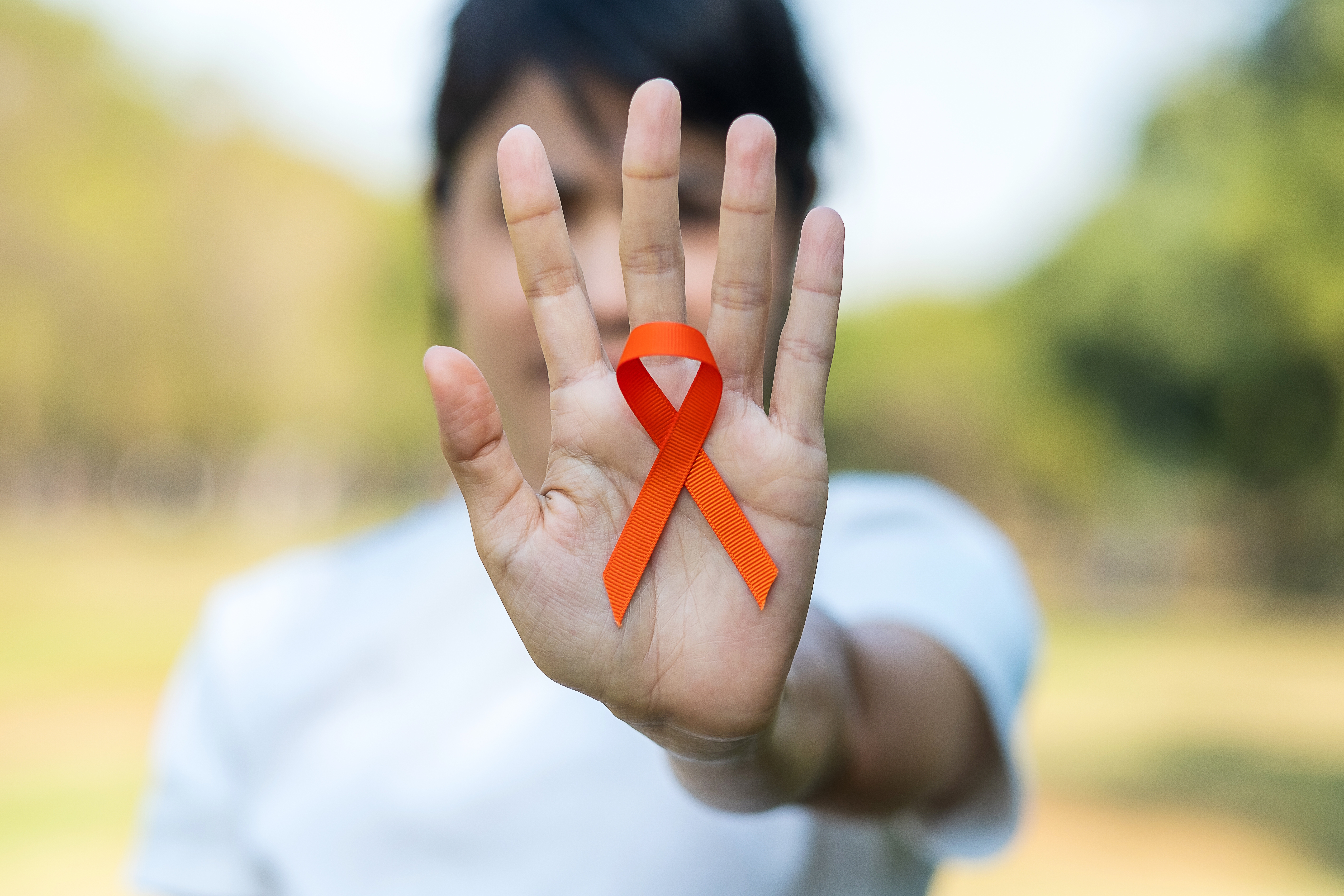 woman holding an orange folded ribbon in support of kidney cancer awareness out in front of her