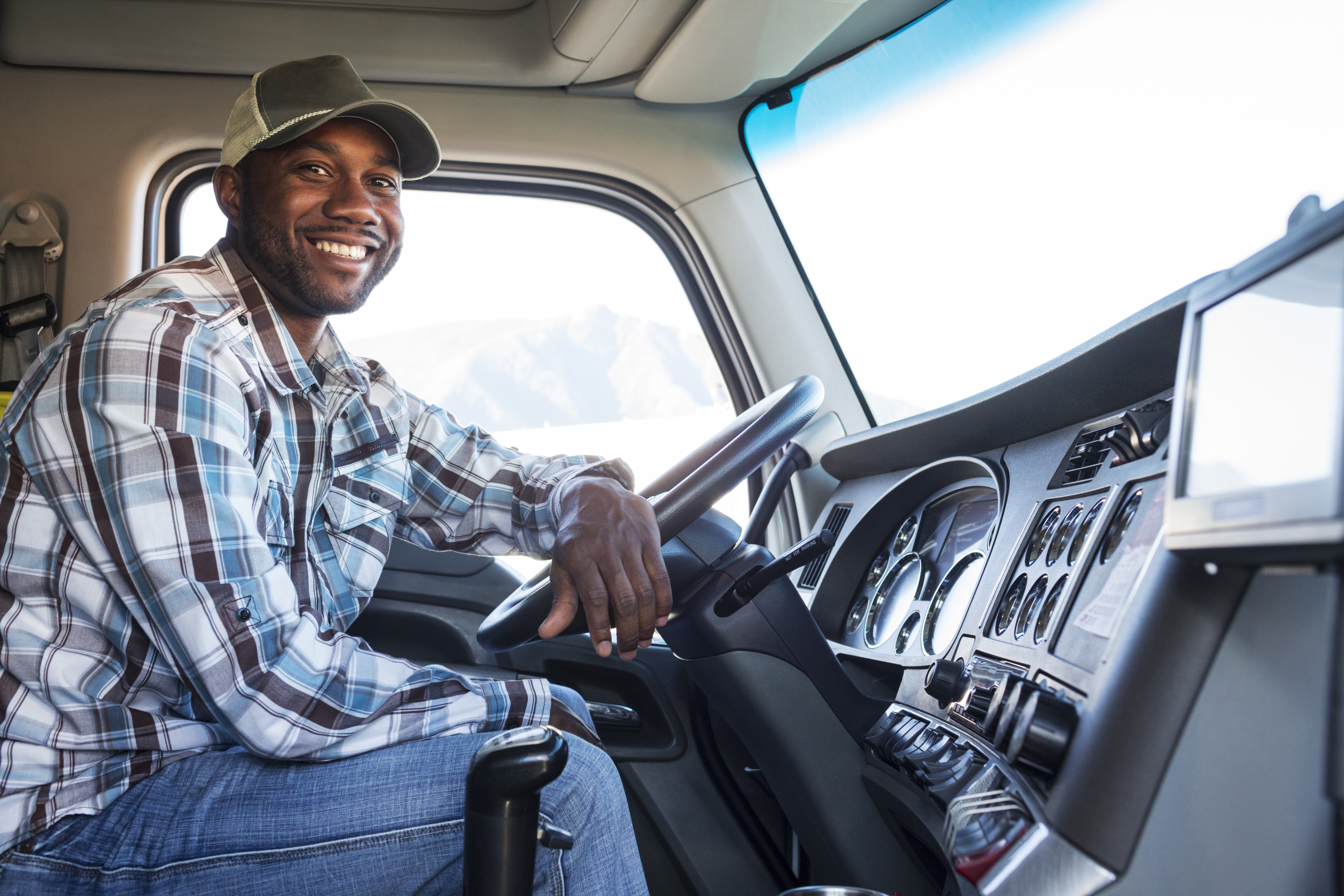 african american man in the driver seat of an 18 wheeler truck smiling facing the passenger side