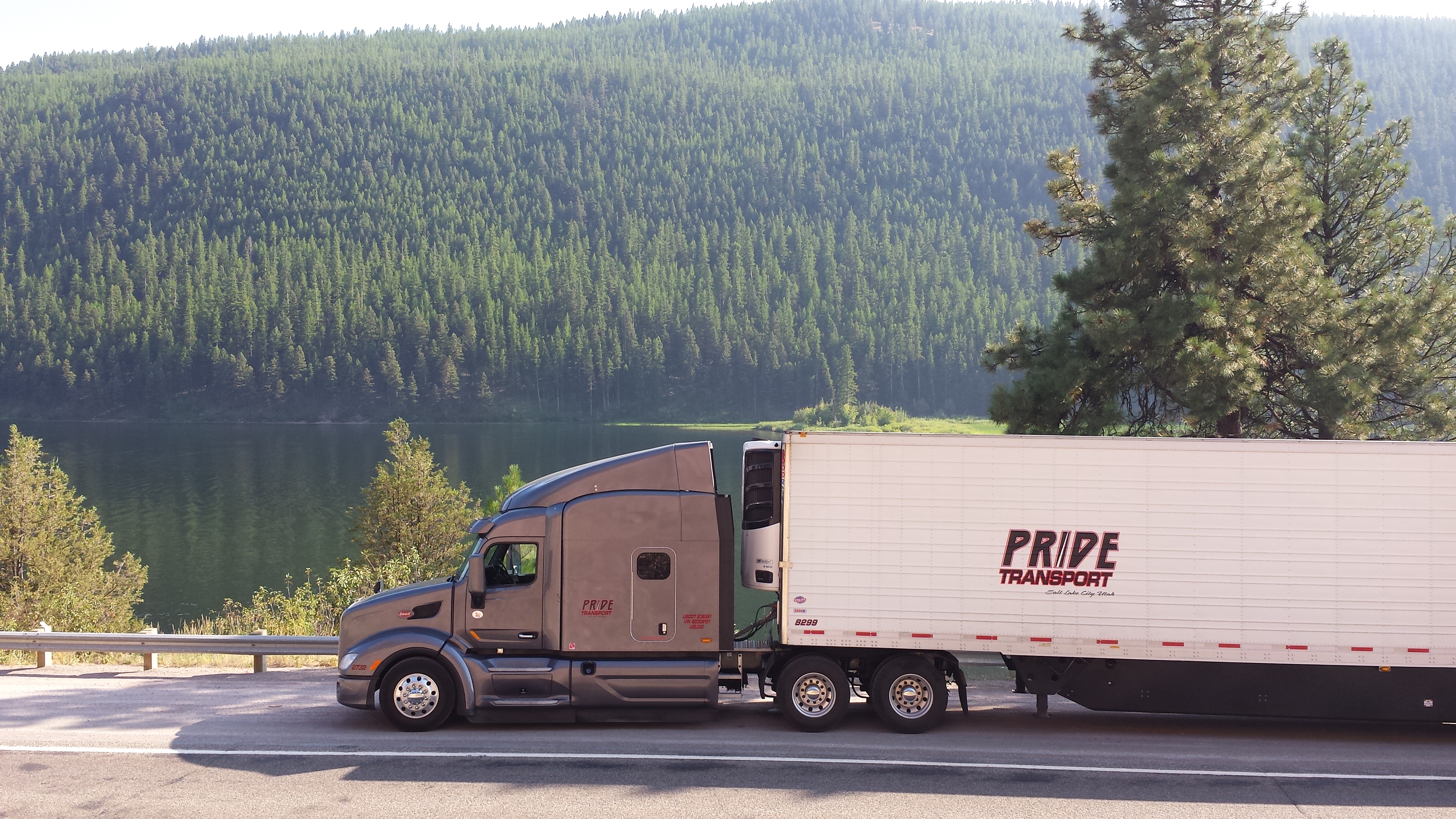 pride transport truck parked with tree line and lake in background
