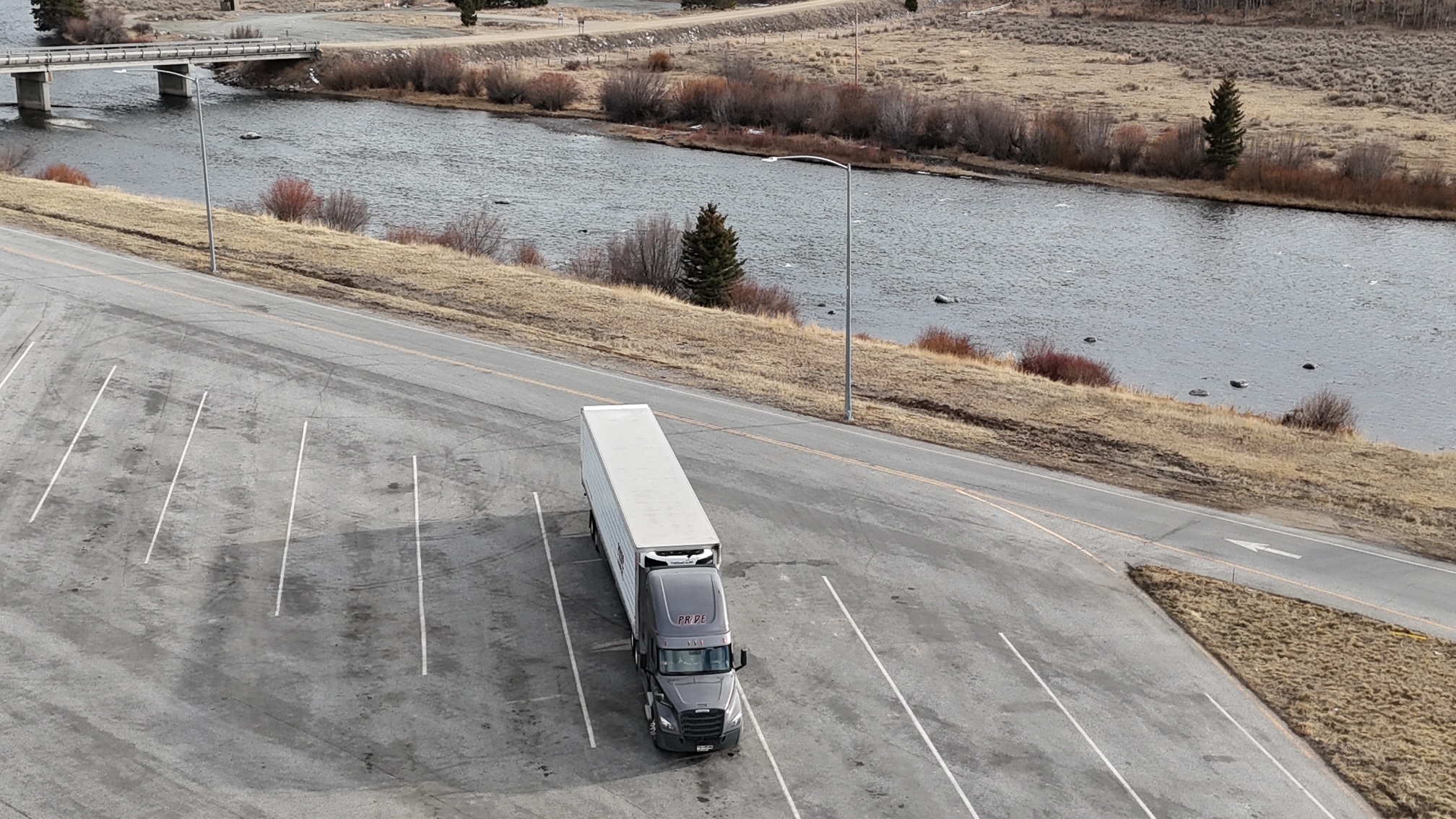 overhead drone photo of pride transport truck in empty parking lot with lake in background