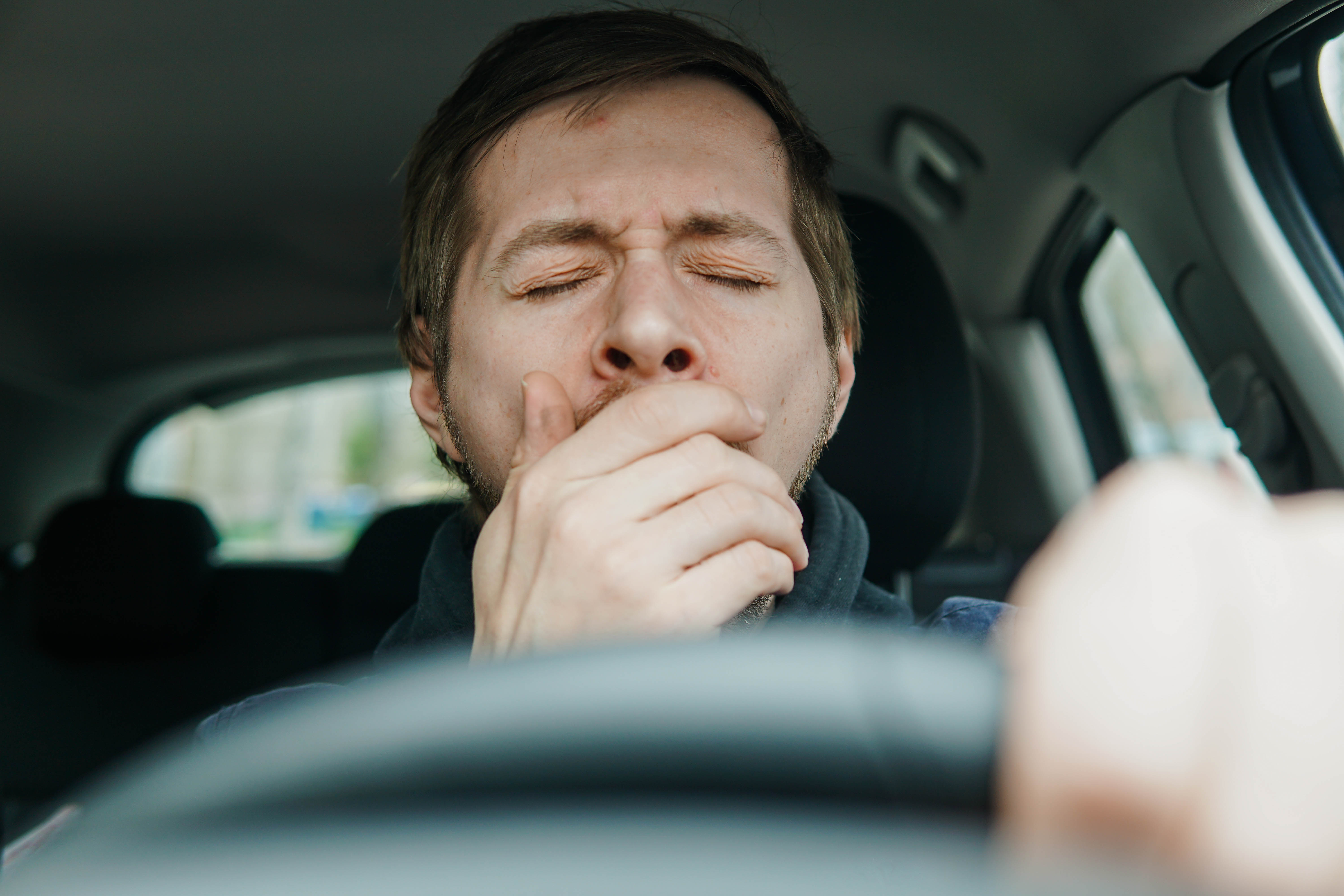 man yawning in the driver's seat of car
