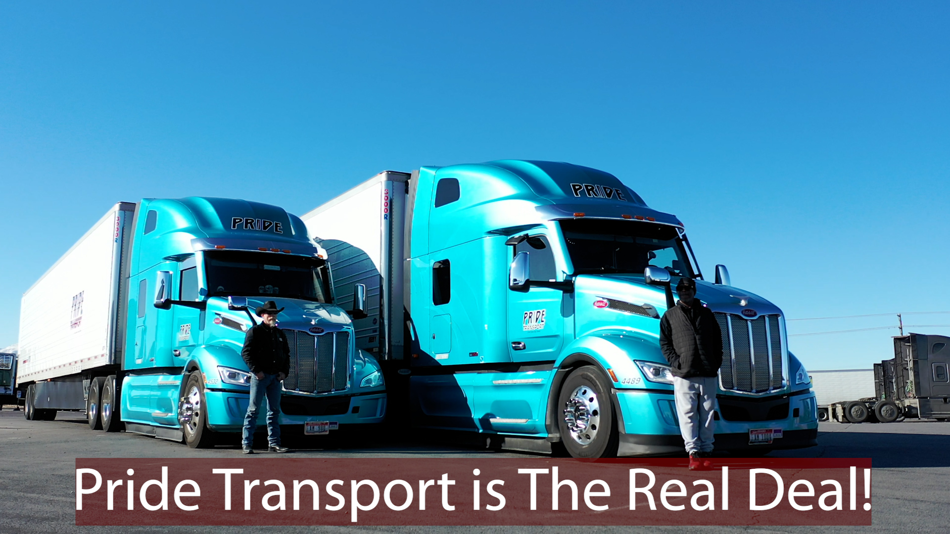 two blue pride transport trucks with drivers standing in front of each