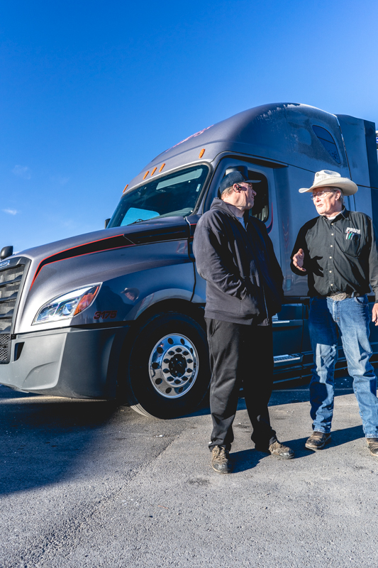 two pride transport employees talking in front of semi