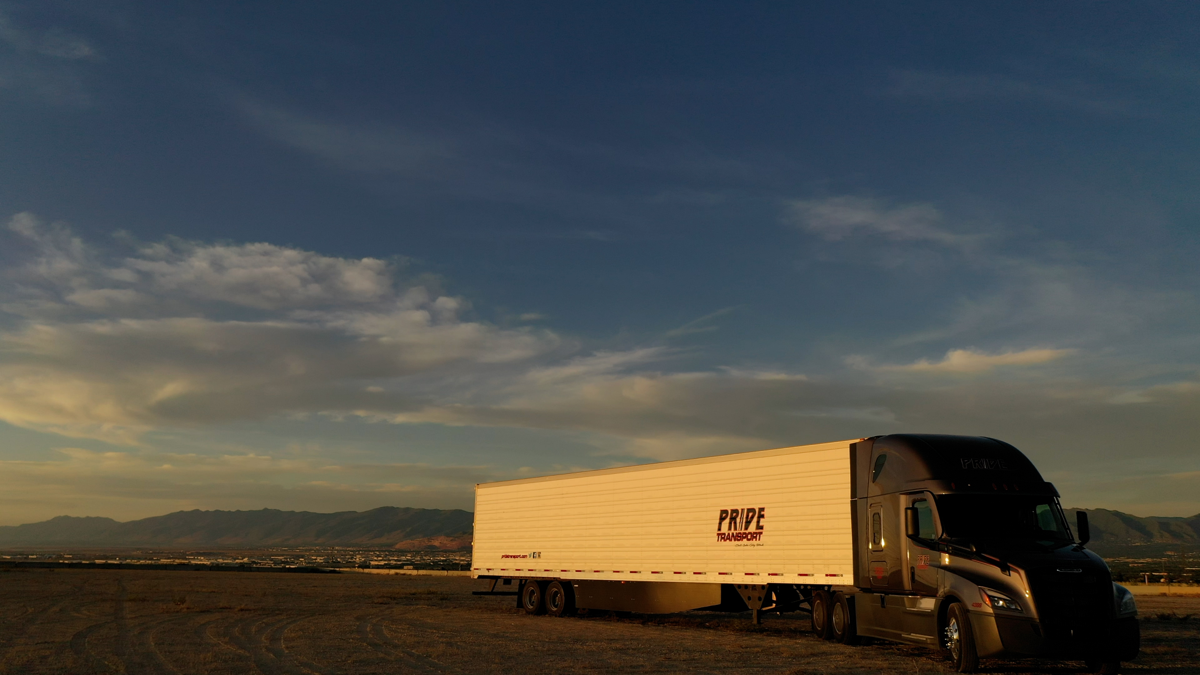Pride Transport truck sitting in an empty dirt lot with a sunset in background