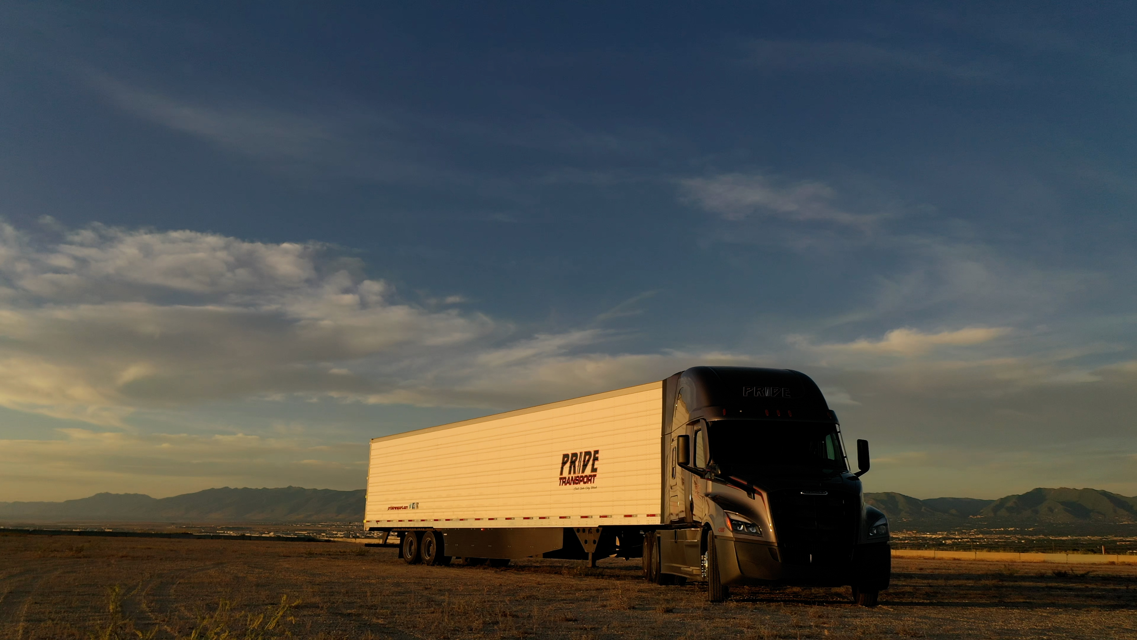 Pride Transport truck parked in a vacant dirt field with mountains in the background