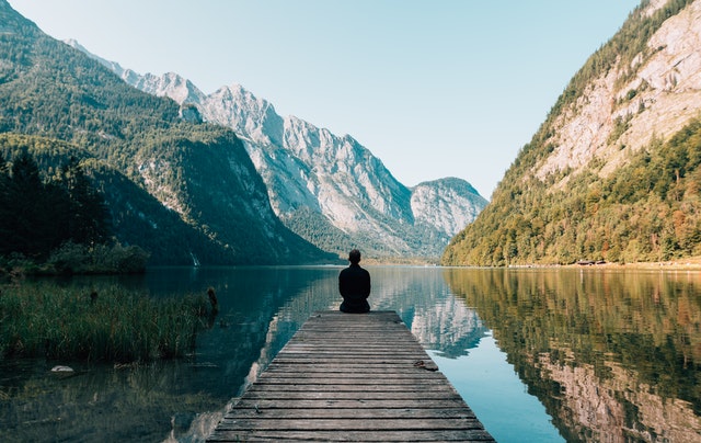 man sitting on dock looking at lake and mountains