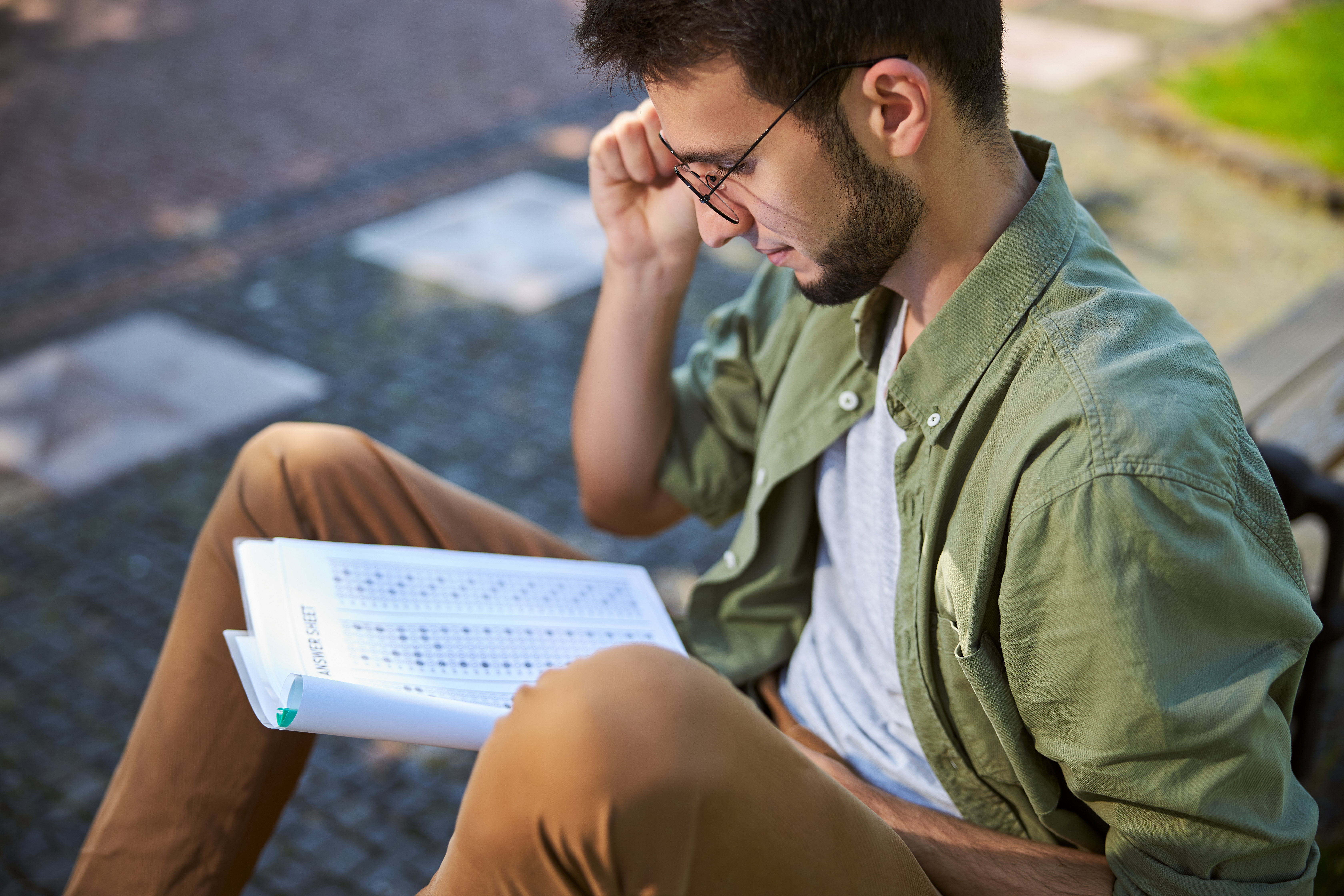 man with glasses sitting outside reading a peice of paper