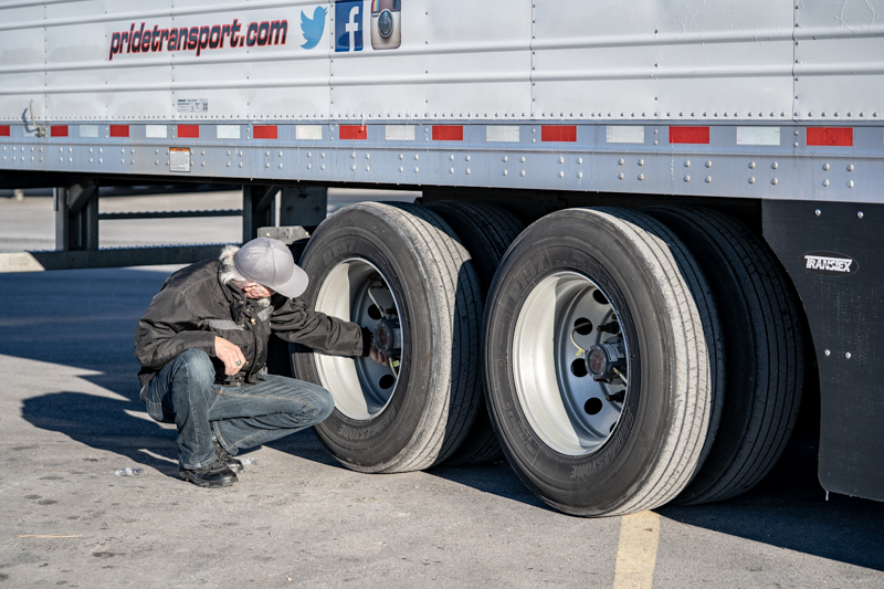 pride transport employee checking tires on semi truck