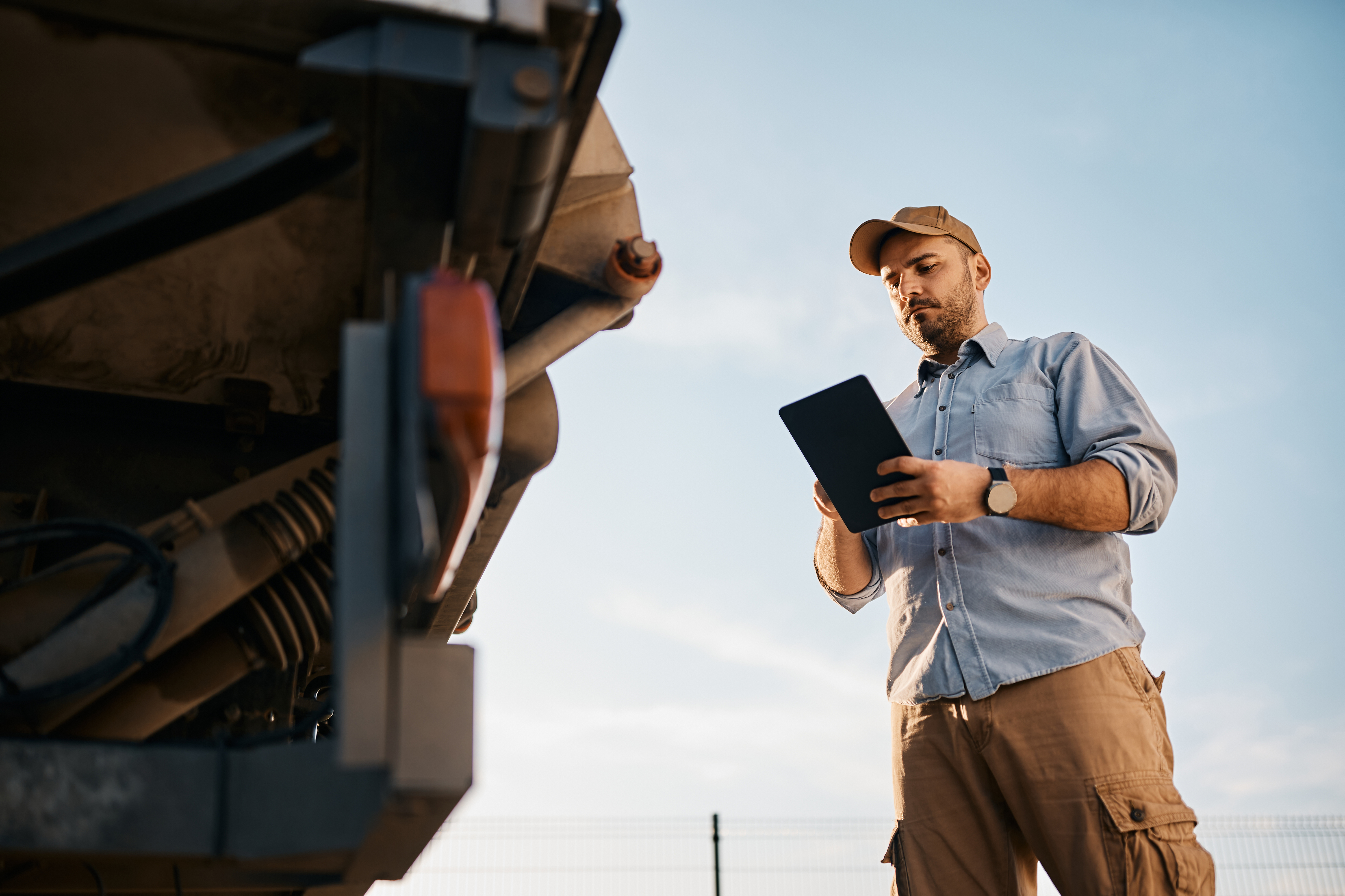 man standing with a tablet device in hand next to the front of 18 wheeler