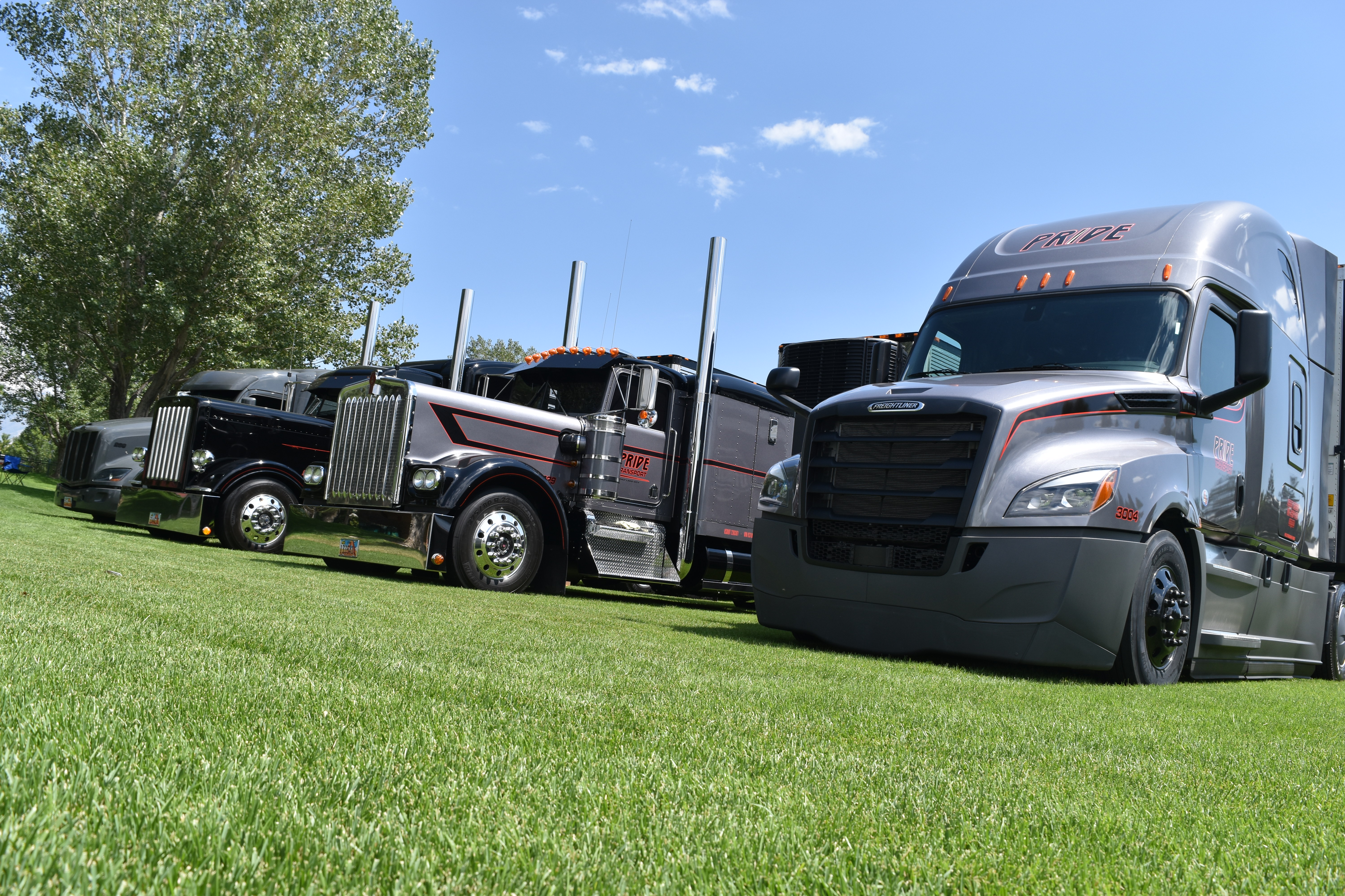 four pride trucks parked in grass at a trade show