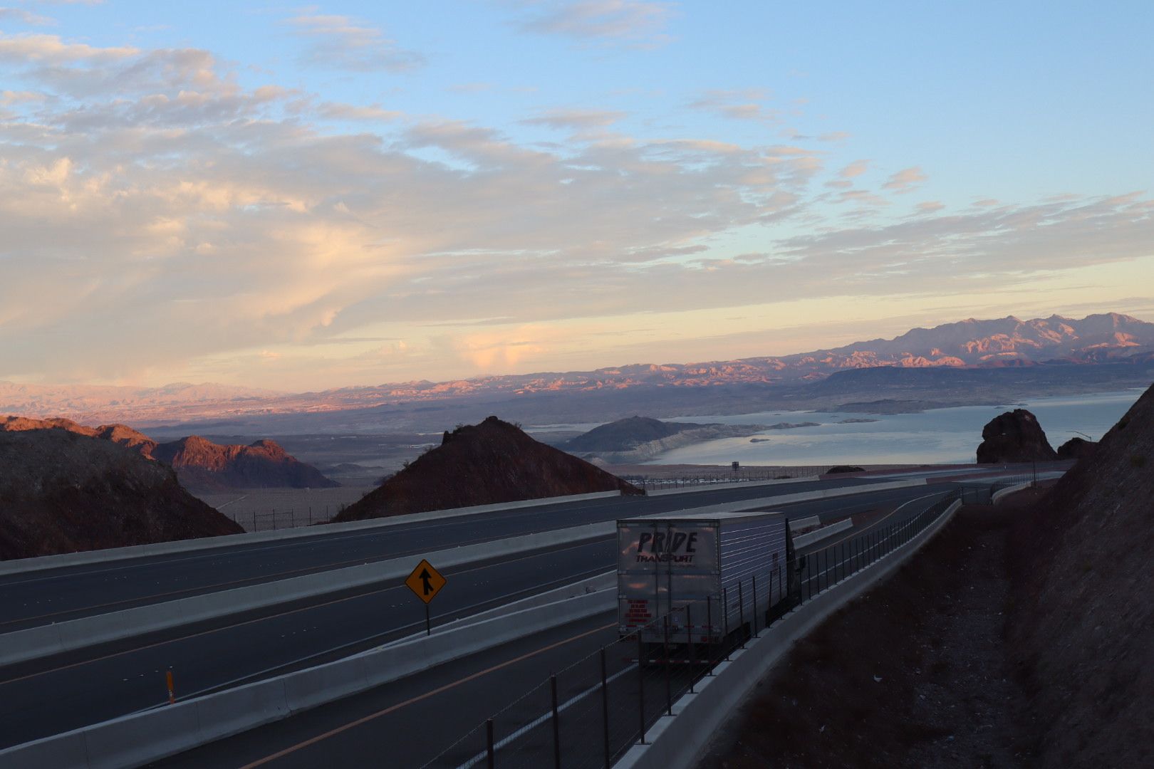 drone photo of pride transport truck driving away on bridge with sunset