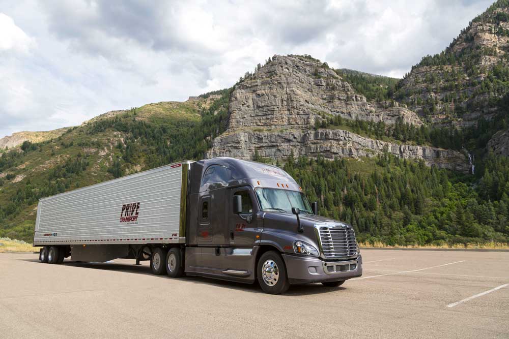 semi truck parked in front of mountain, rocks and trees