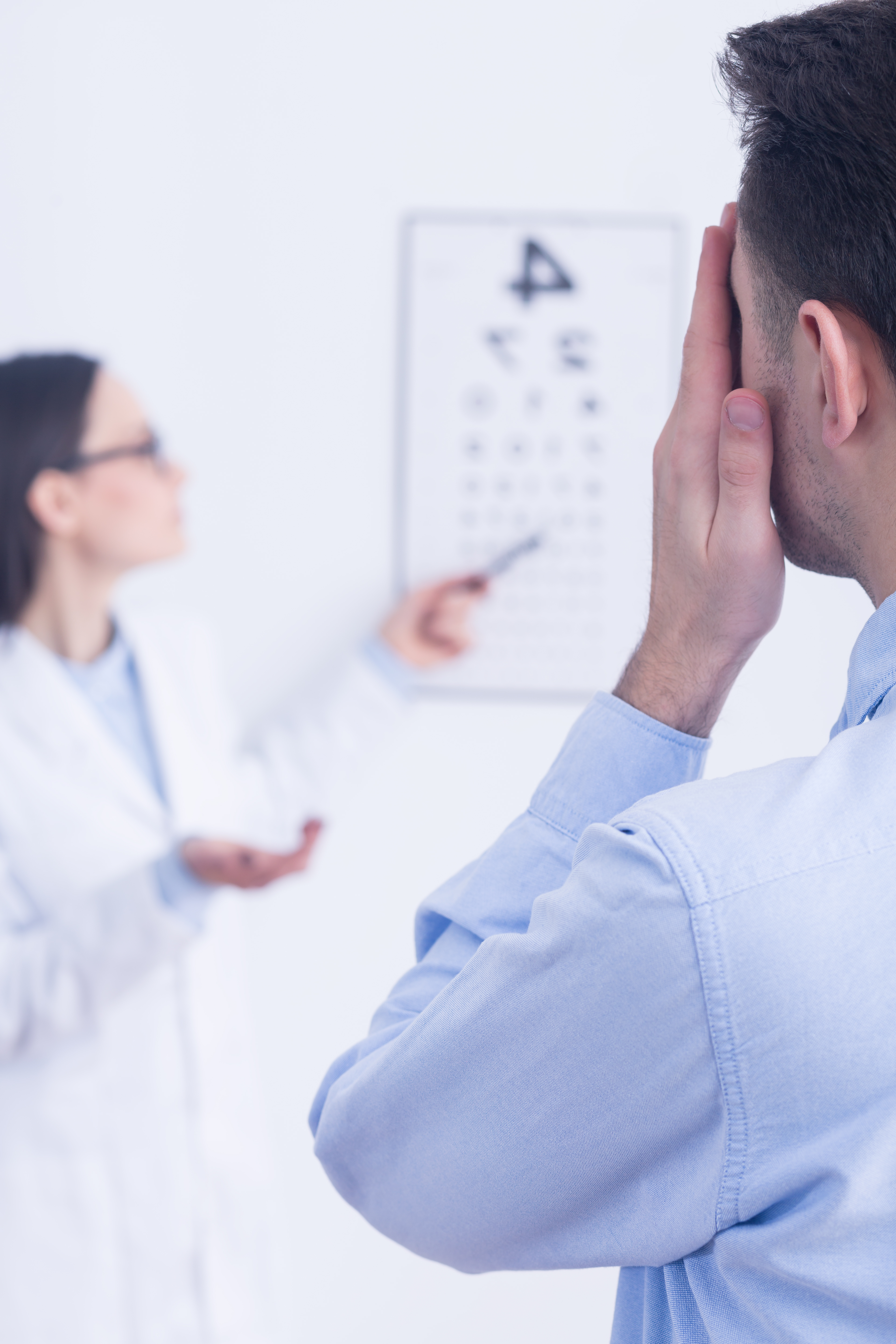 man holding one eye closed at the eye doctor reading an eye test