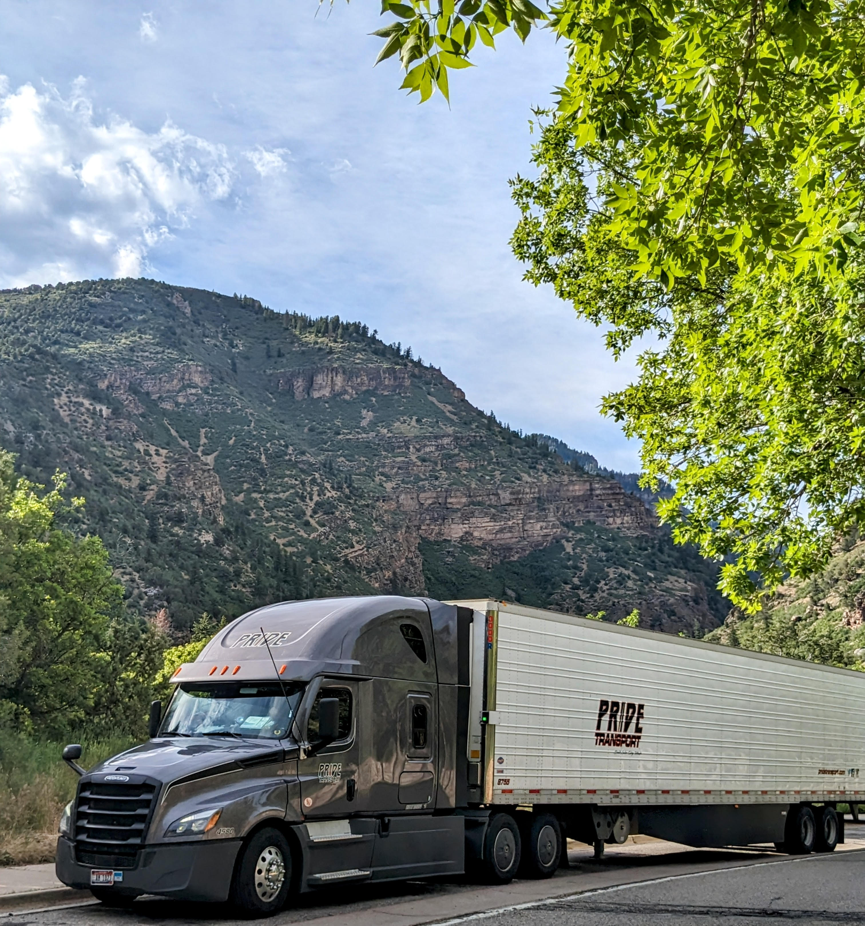 pride transport truck parked in front of green mountainscape
